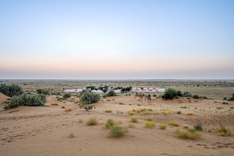 Desert sunset over a camel caravan and tents in Jaisalmer, India, showcasing serene arid landscapes.